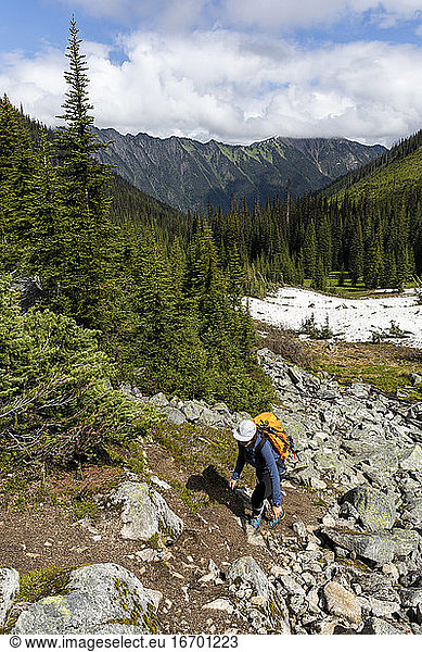 hiker climbing stony slope while travelling in mountainous terrain