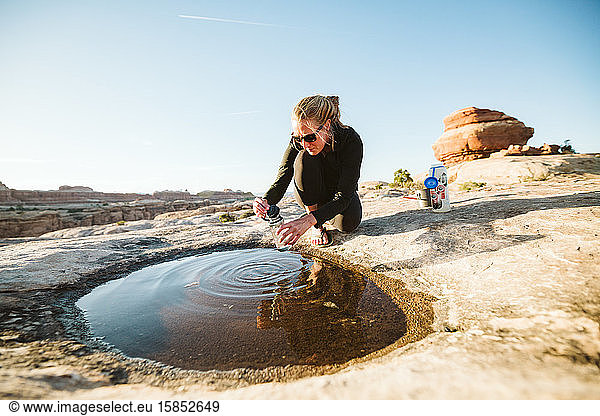 hiker collects drinking water from a shallow puddle in the desert