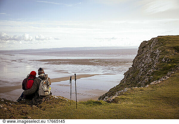 Hiker couple taking a break on cliff over tranquil winter ocean beach