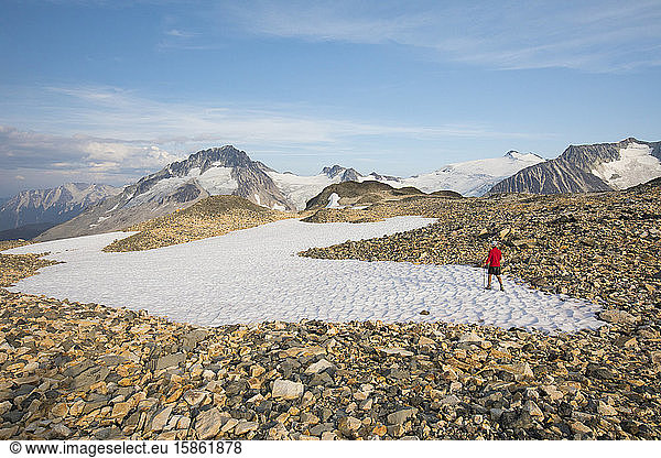 hiker crossing snow patch in rocky terrain.