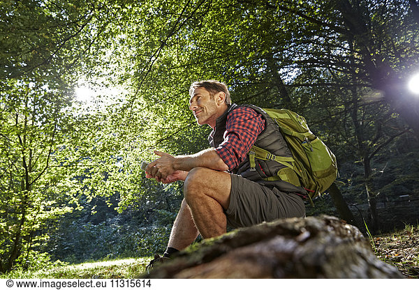 Hiker in forest sitting on tree trunk, holding smart phone
