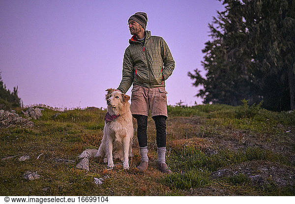 Hiker in puffy coat scratching dog ear at sunset