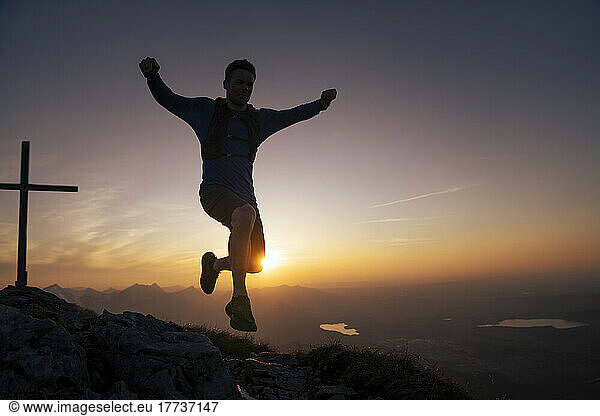 Hiker jumping on mountain peak at sunset
