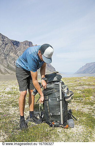Hiker leans over to zip up backpack his large  heavy backpack.