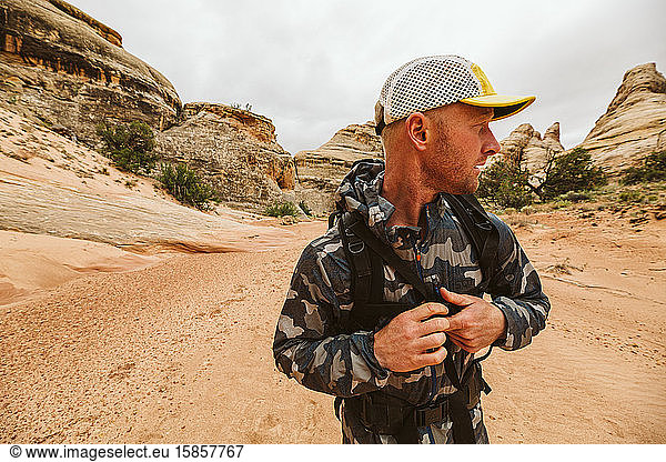 hiker looks left and buckles his chest strap of backpack in desert