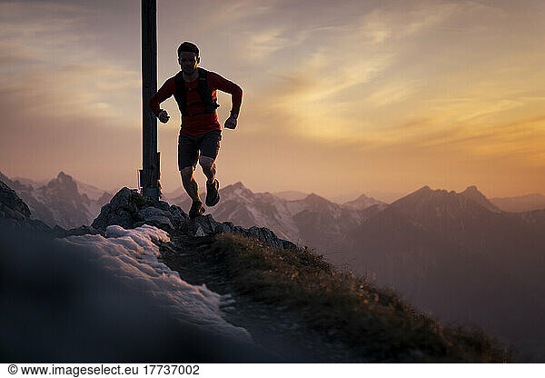 Hiker running on top of Sauling mountain peak at sunset
