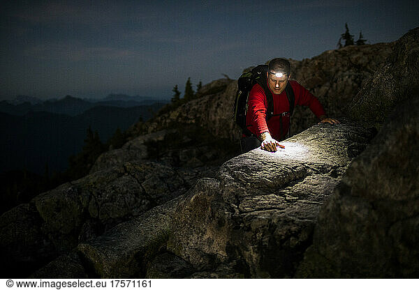 Hiker scrambling on mountain ridge using headlamp.