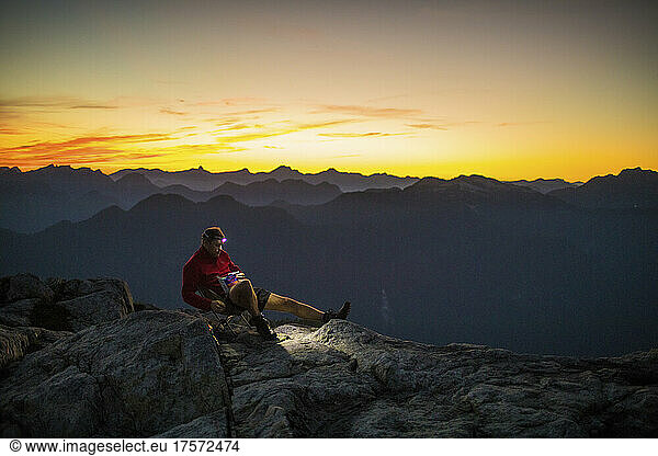 Hiker sitting on mountain summit  enjoying the sunrise.
