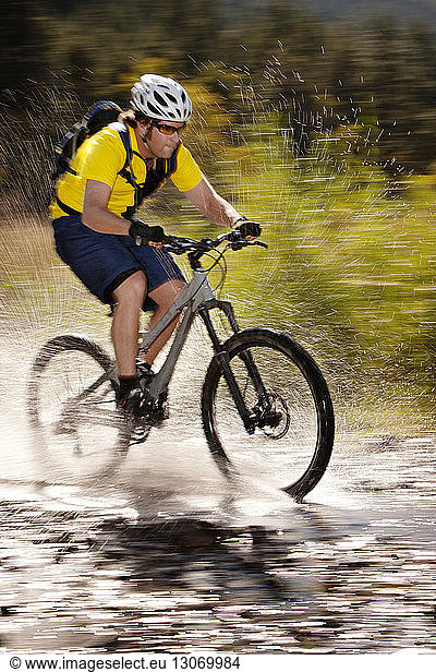 Hiker splashing water while riding bicycle in puddle