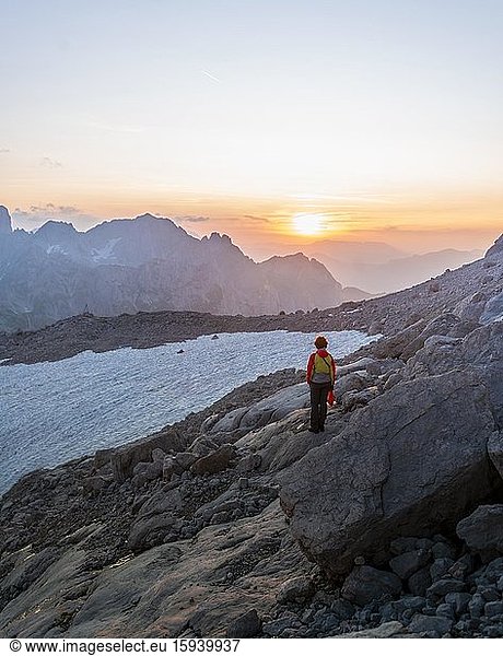 Hiker stands in rocky alpine terrain and looks at sunset over Gosaukamm with mountain peak Bischofsmütze  evening mood  Salzkammergut  Upper Austria  Austria  Europe