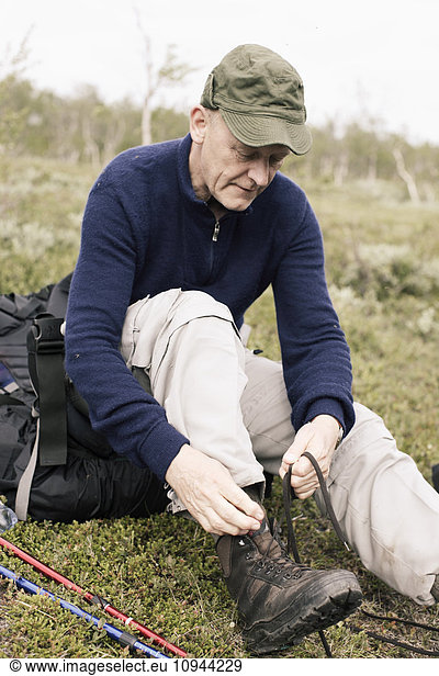 Hiker tying shoelace while sitting on landscape