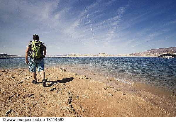 Hiker walking on sea shore against sky