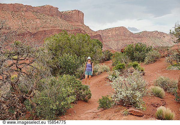 hiker walks on red dirt path amongst desert plants near moab utah