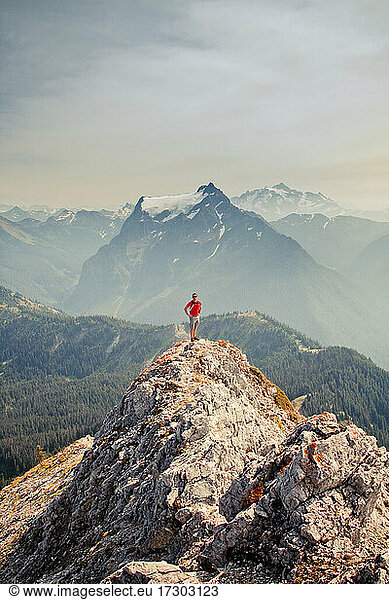 Hiker wearing red shirt stands on mountain top with scenic view behind
