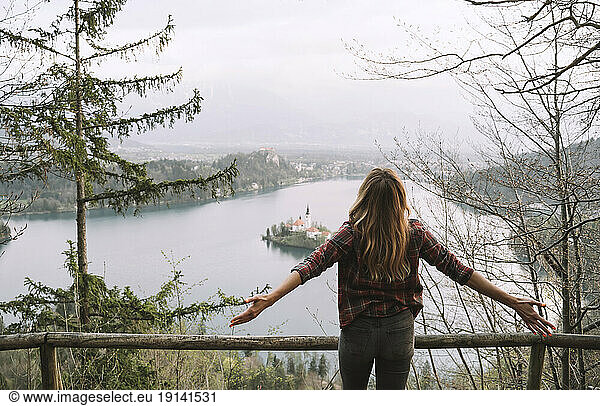 Hiker with arms outstretched standing near railing facing sea