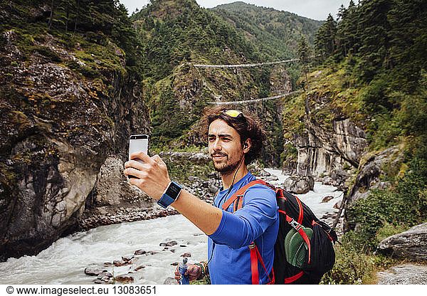Hiker with backpack taking selfie while standing by river at Sagarmatha National Park