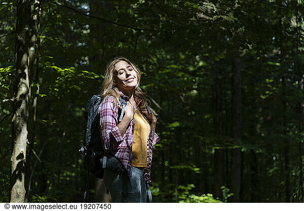 Hiker with eyes closed enjoying sunlight in forest