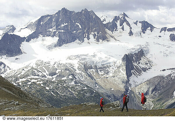 Hikers on a ridge line with snow covered peaks in the background; Adamants Mountain Range  British Columbia  Canada