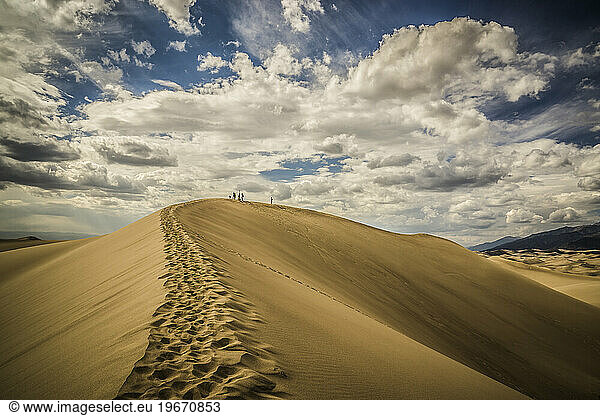 Hikers on top of a sand dune with puffy clouds on a sunny day.