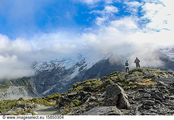 Hikers taking in view surrounded by glacial mountains in the clouds.