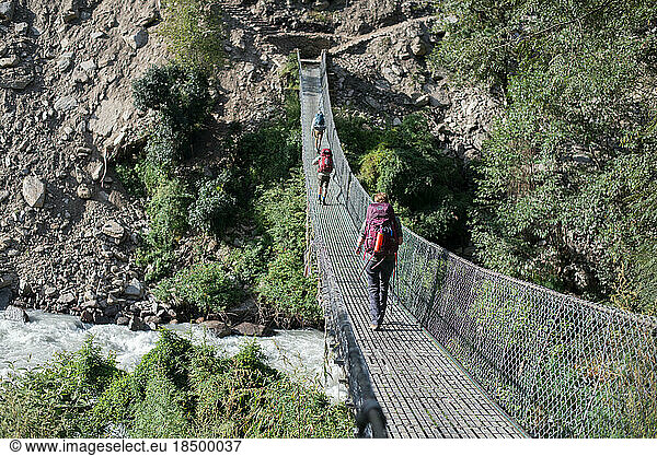 Hikers walking on skinny bridge over canyon and river in Asia
