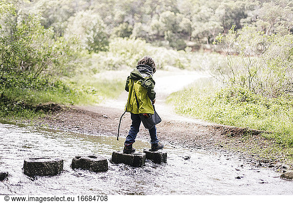 Hiking kid wearing raincoat crossing a river
