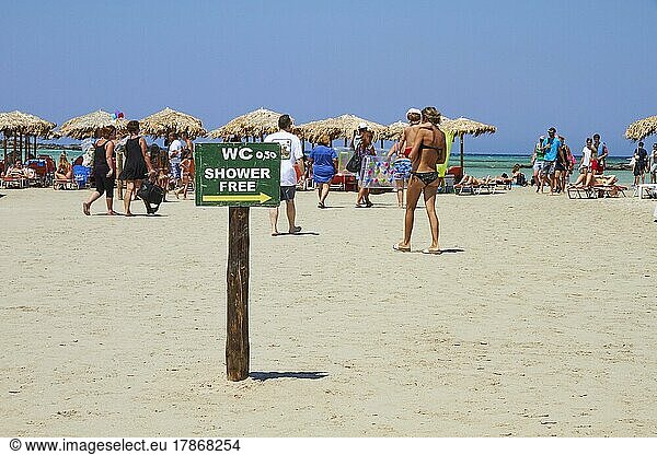 Hinweisschild WC  Touristen  Sonnenschirme  blauer wolkenloser Himmel  Sandstrand  Strand von Elafonissi  Südwest-Kreta  Insel Kreta  Griechische Inseln  Griechenland  Europa
