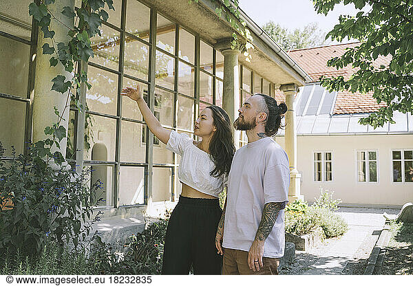 Hipster couple examining plants outside house