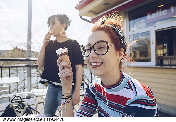 Hipster female friends eating ice cream by shop