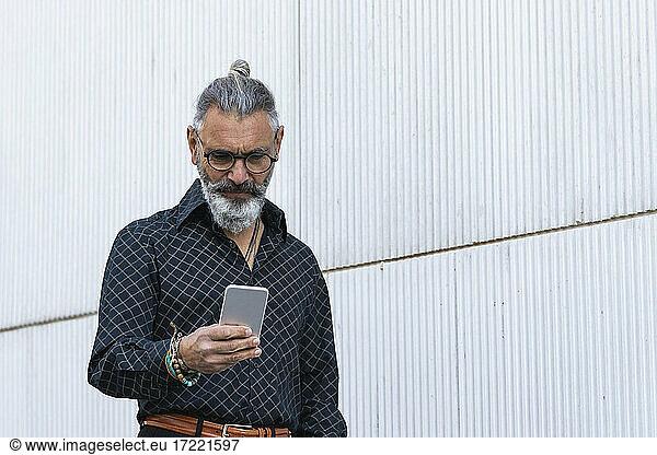 Hipster-Geschäftsmann mit Smartphone an der Wand