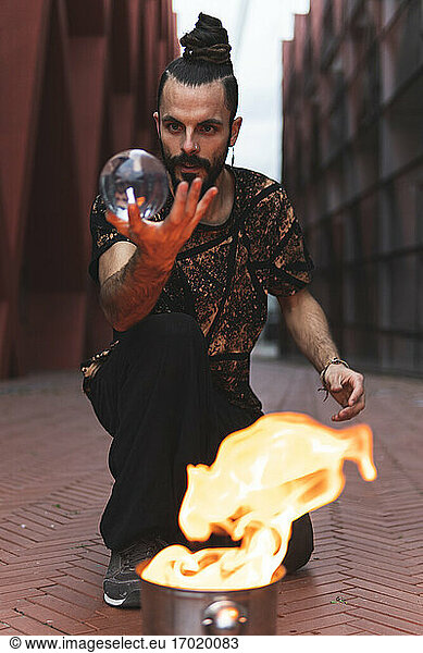 Hipster-Mann mit Acrylkugel beim Feuerkunststück auf dem Fußweg