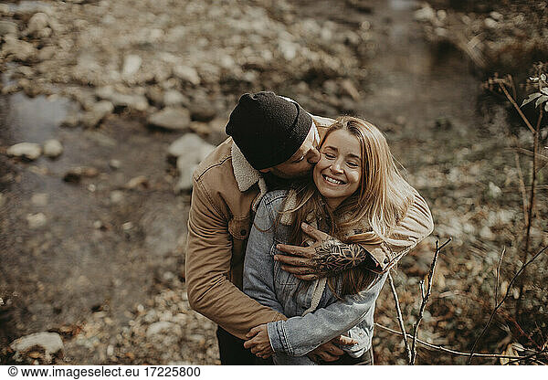 Hipster-Mann mit Strickmütze küsst Freundin im Wald