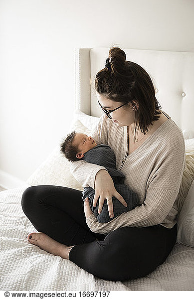 Hipster Millenial Mom Smiles Down at Swaddled Newborn Son