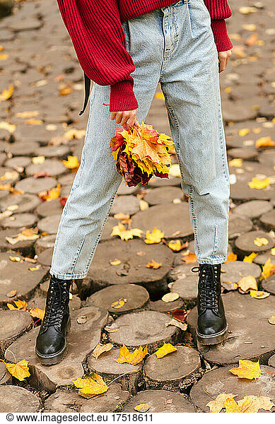 Hipster stylish girl standing and holding maple leaves in hand