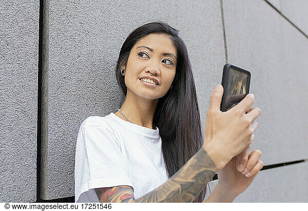 Hipster woman looking away holding smart phone by wall