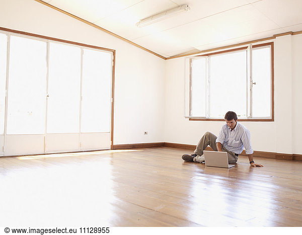 Hispanic businessman using laptop on floor in empty office