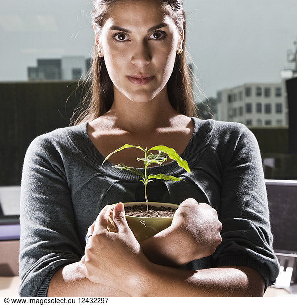 Hispanic woman holding a house plant in an office cubicle.