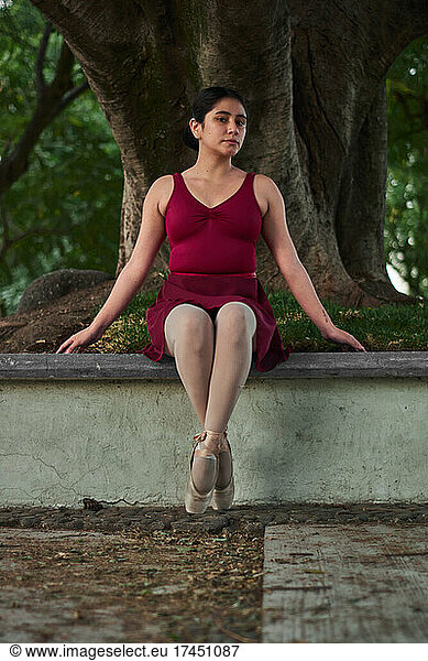 Hispanic young woman practices ballet with pointe shoes in a park.