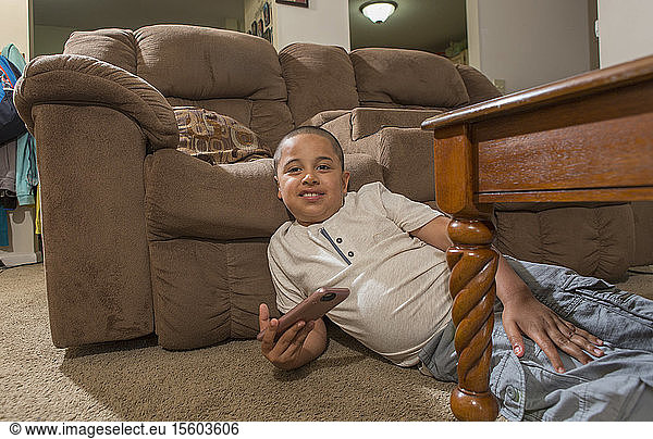 Hispanischer Junge mit Autismus spielt ein elektronisches Spiel auf seinem Handy im Wohnzimmer