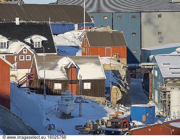 Historische Gebäude neben der modernen Fischfabrik. Winter im zugefrorenen Hafen der Stadt Ilulissat am Ufer der Diskobucht.Nordamerika  Grönland  Dänemark