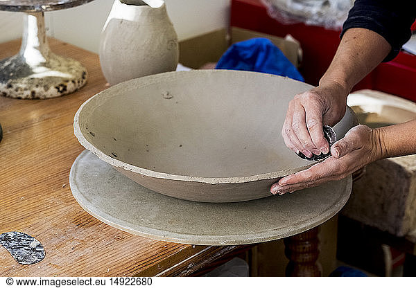 Hochauflösende Nahaufnahme einer Keramikkünstlerin in ihrer Werkstatt  die an einer Tonschale arbeitet.