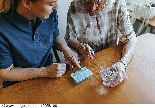 Hochformatige Ansicht einer weiblichen Pflegekraft  die einer älteren Frau zu Hause die Medikamentendosis erklärt