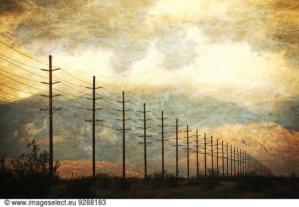 Hochspannungsleitungen in Reihen quer durch die Landschaft  vor einem untergehenden Himmel.