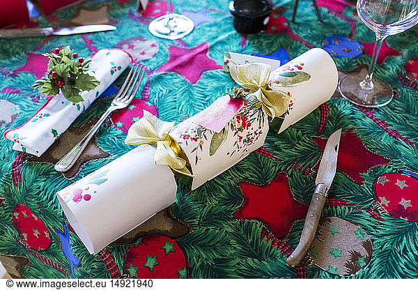 Hochwinkel-Nahaufnahme von Besteck und weißem Weihnachts-Cracker auf grüner und roter Tischdecke mit weihnachtlichen Motiven.