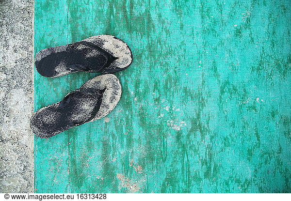 Hochwinkel-Nahaufnahme von sandig-schwarzen Flip-Flops auf türkisfarbener Bodenmatte.