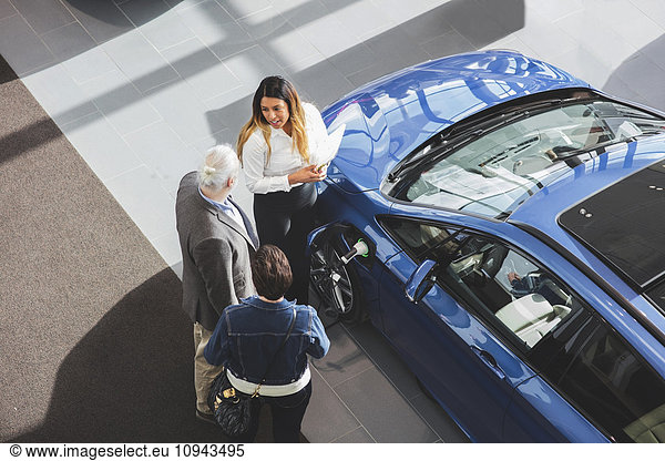 Hochwinkelansicht der Verkäuferin  die dem Kunden das Auto im Showroom zeigt.