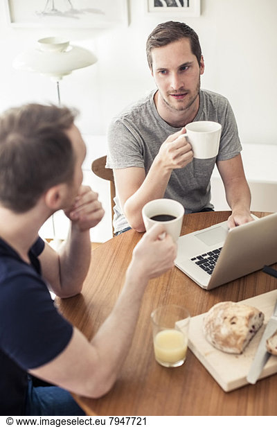 Hochwinkelansicht des homosexuellen Paares beim Frühstück mit Laptop am Tisch