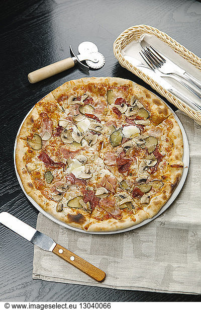 Hochwinkelansicht einer Pizza im Teller mit Besteck und Serviette auf dem Tisch