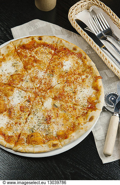 Hochwinkelansicht einer Pizza mit Besteck und Serviette auf dem Tisch