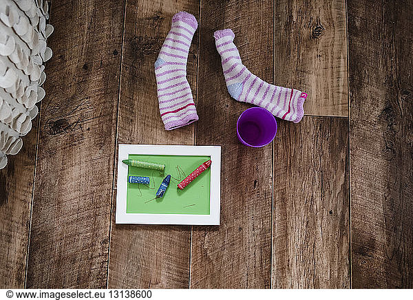 Hochwinkelansicht einer Schreibtafel mit Buntstiften nach Behälter und Socken und Hartholzboden